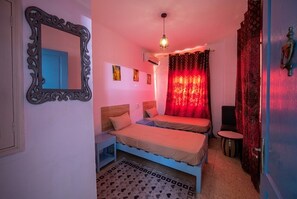 A room with two beds, a mirror, a hanging light fixture, and a patterned rug.