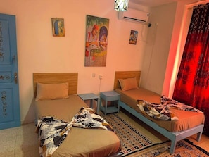 A room with two beds, a blue wardrobe, and a wall-mounted air conditioner.