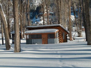 Eine Holzhütte, umgeben von verschneitem Gelände und Bäumen.