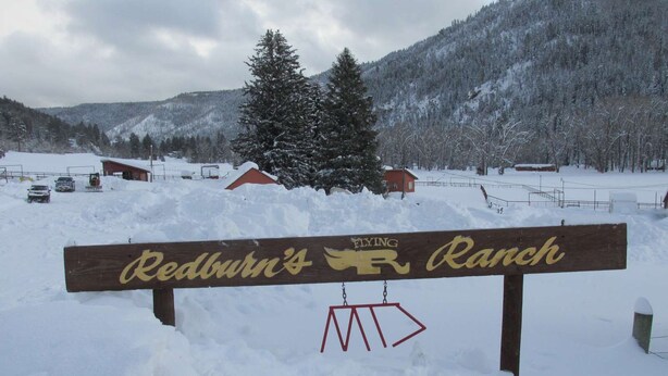 Een houten bord met 'Redburn's Ranch' en een vliegende vogel logo, omgeven door een besneeerd landschap en bergen.