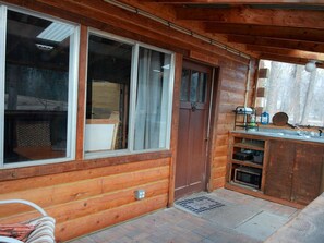 Una cabaña de madera con un ventanal grande, una puerta y una kitchenette con fregadero y estufa.