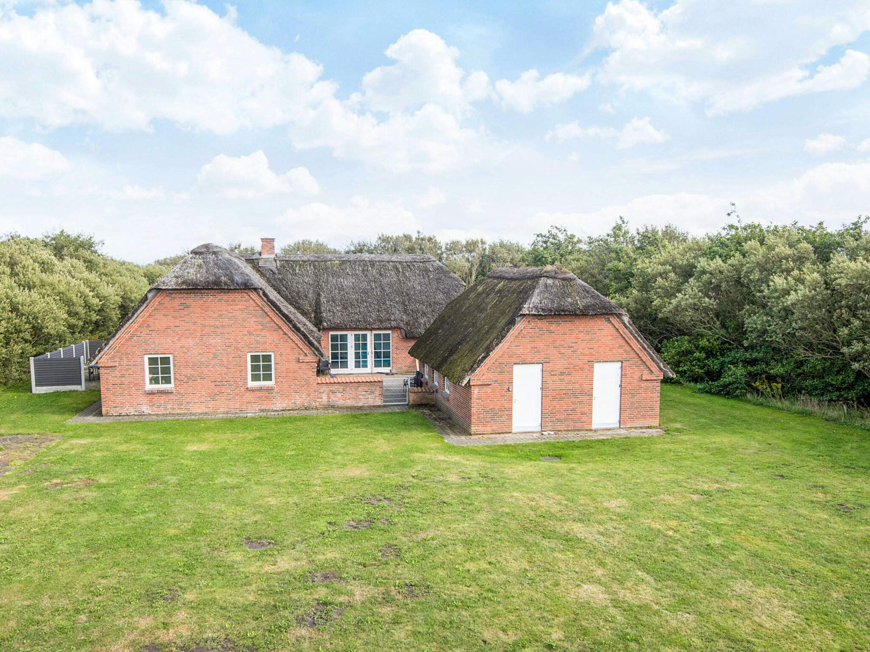 A traditional brick house with a thatched roof, a small attached shed, and a grassy lawn.
