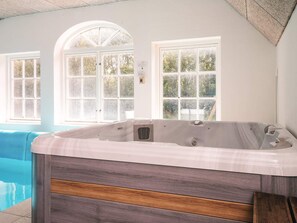 A spa room with a hot tub, large windows, and a view of a swimming pool. - 4 Star Holiday Home in Ulfborg (Ulfborg)