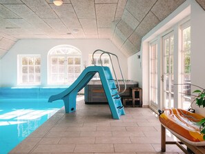 A swimming pool with a blue slide, a sunlit room with large windows, and a bench with a colorful inflatable float. - 4 Star Holiday Home in Ulfborg (Ulfborg)