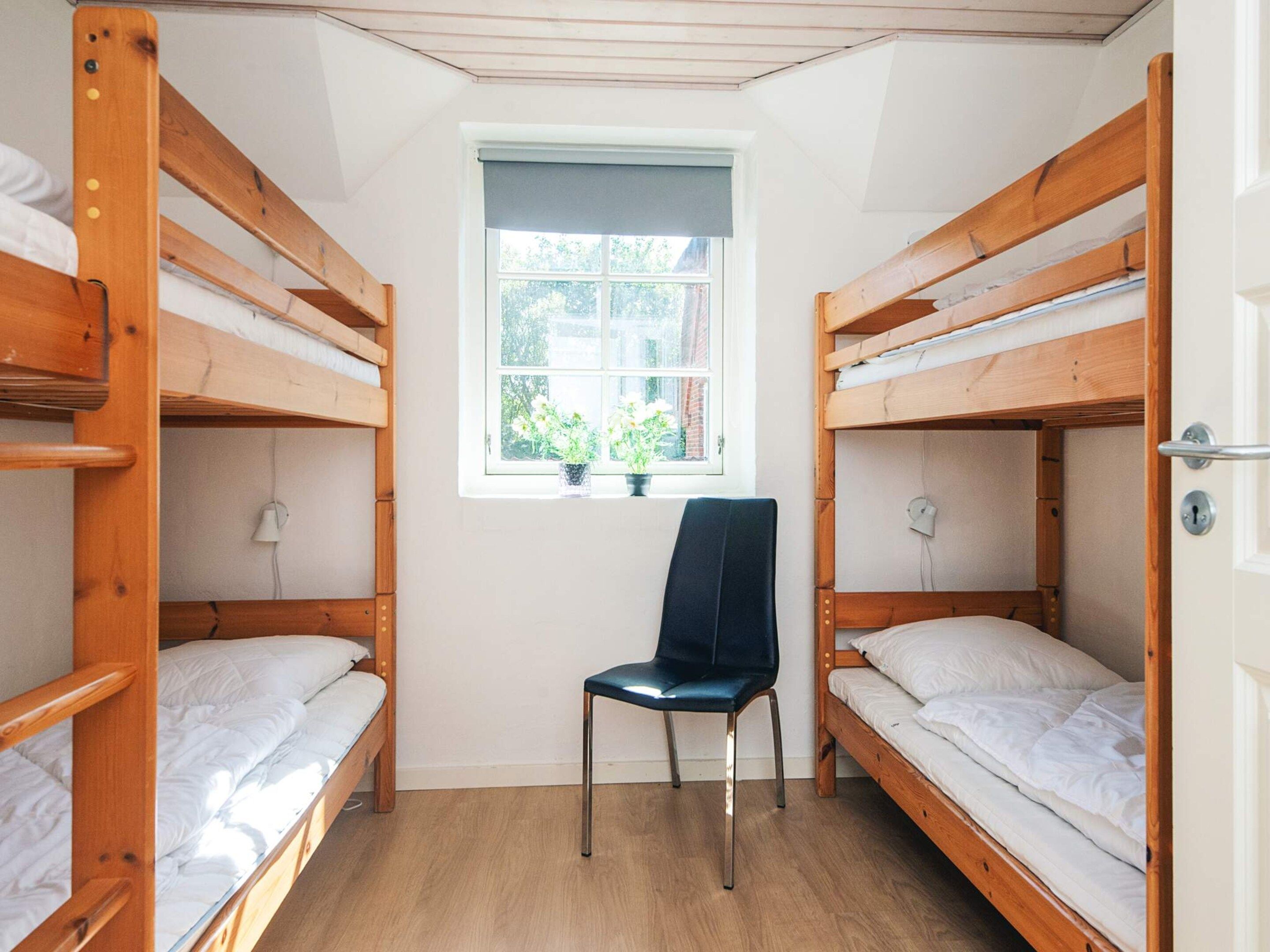 A room with two bunk beds, a chair, a window with a view of greenery, and a door with a lock.