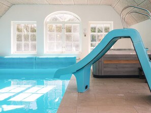 An indoor swimming pool with a slide, large windows, and a wooden bench. - 4 Star Holiday Home in Ulfborg (Ulfborg)