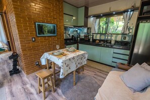 A compact kitchen with a dining area, a single bed, and a view of greenery through the window. - Studio da Mata de Nova Friburgo (Nova Friburgo)
