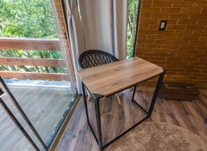 A wooden table with metal legs in a room with a brick wall and a sliding glass door leading to an outdoor area. - Studio da Mata de Nova Friburgo (Nova Friburgo)