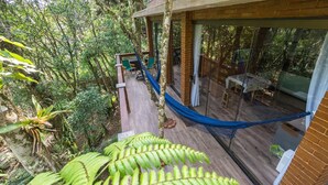 A wooden deck with a hammock, a table, and chairs, surrounded by dense foliage.