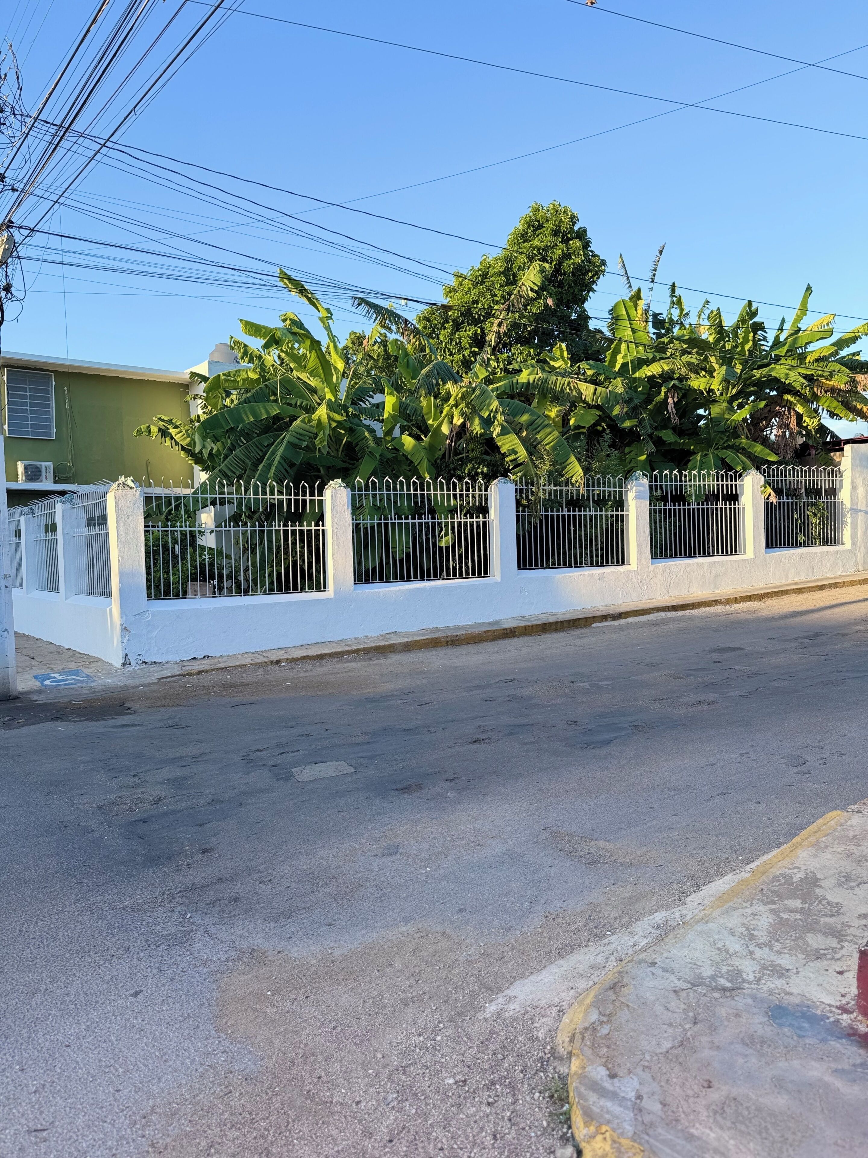 A street with a white fence, a clear blue sky, and a building with a green wall.