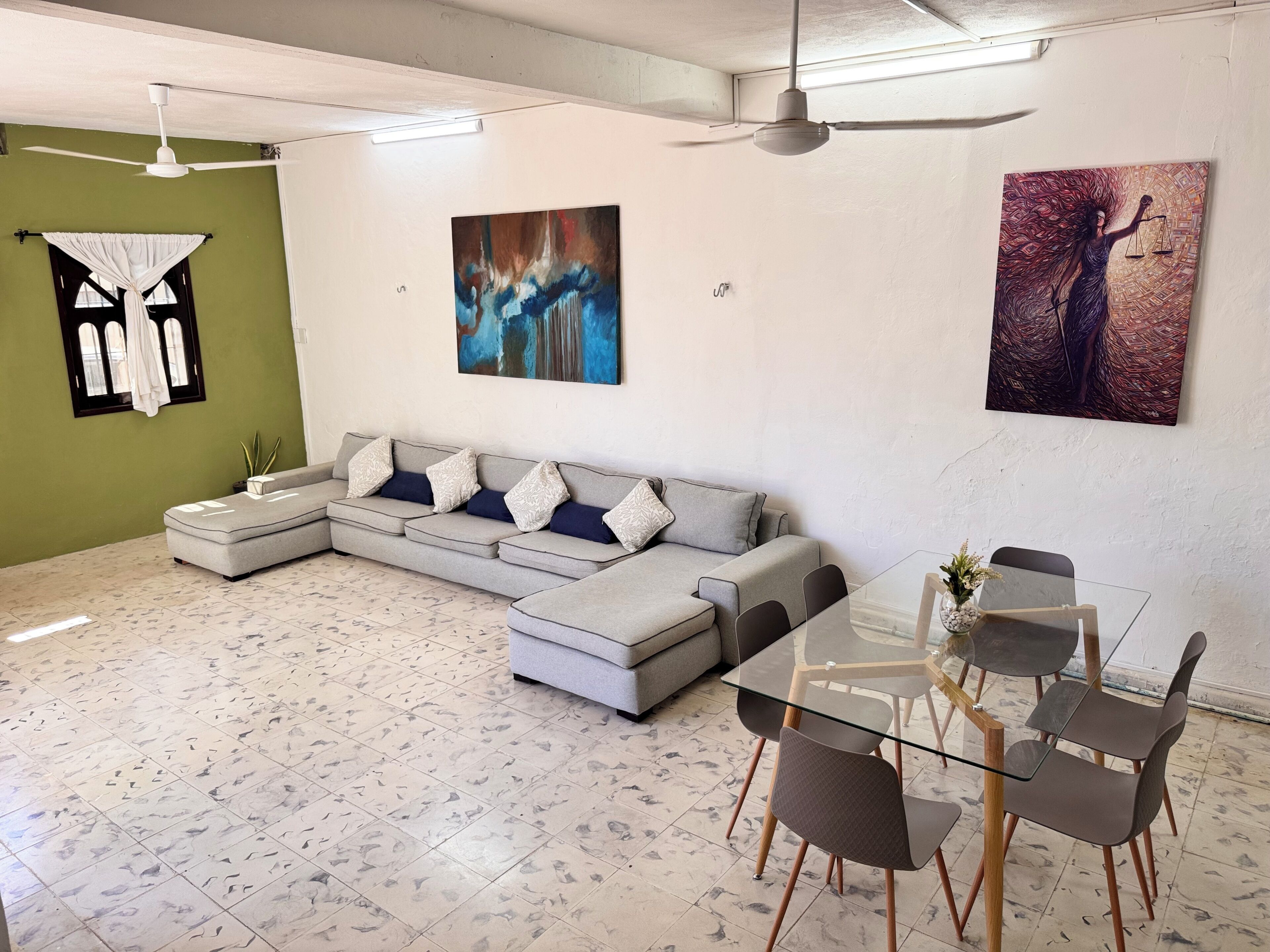 Un salon comprenant un canapé d’angle, une table à manger en verre avec des chaises, et des œuvres d’art accrochées aux murs.