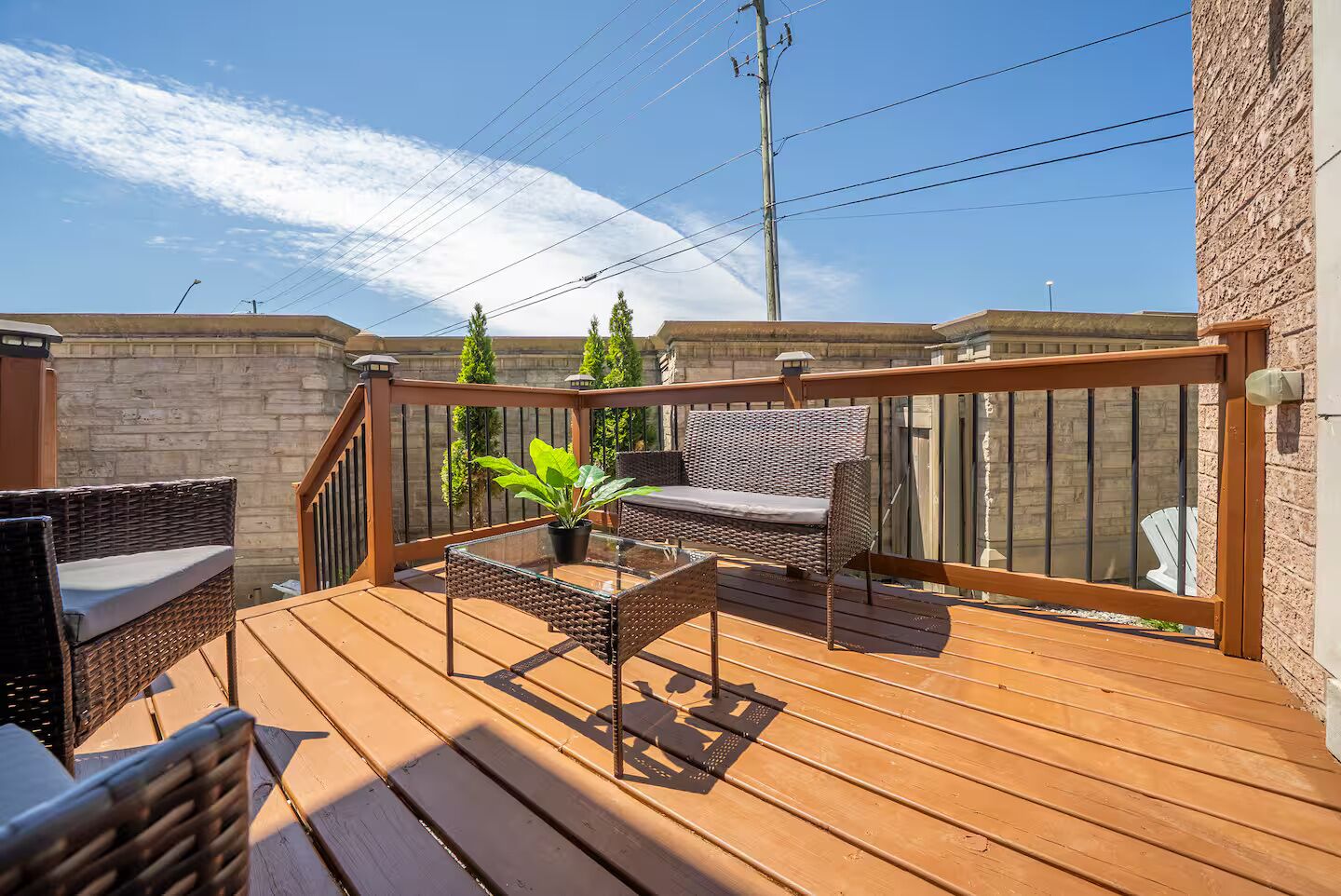 Une terrasse en bois avec des meubles en osier, une table en verre et une plante en pot.