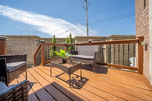 A wooden deck with wicker furniture, a glass table, and a potted plant.