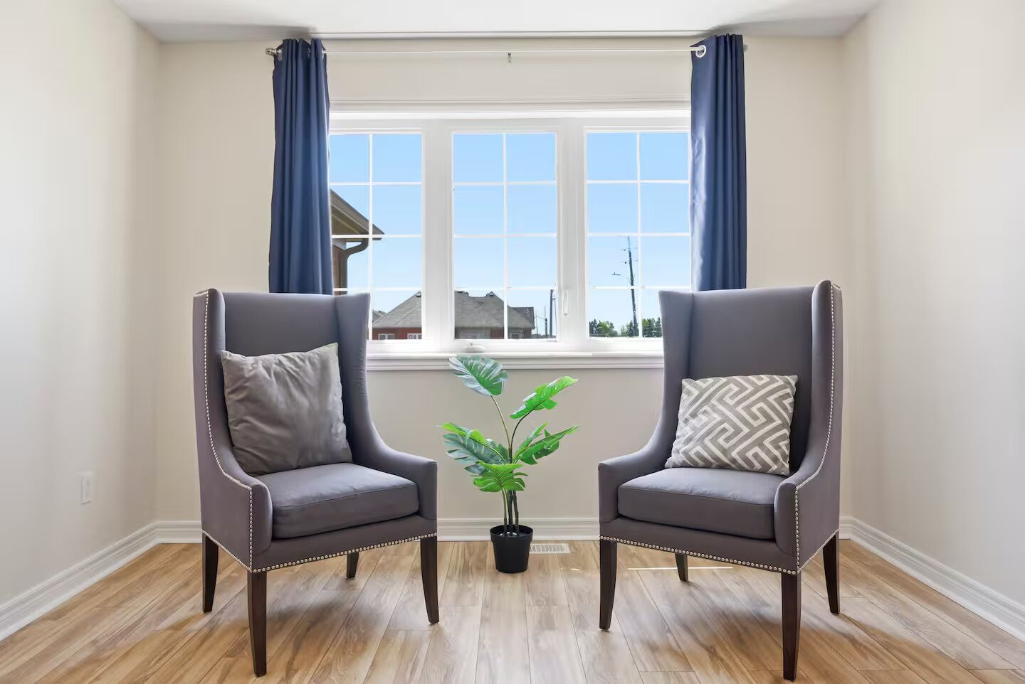 Ein Zimmer mit zwei Sesseln, einer Zimmerpflanze und einem Fenster mit Vorhängen.
