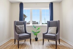 Une pièce avec deux fauteuils, une plante en pot et une fenêtre avec des rideaux.