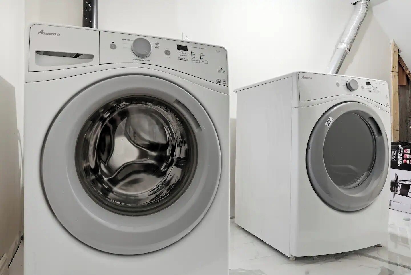 Vue de face d’un lave-linge Amana à chargement frontal, de couleur blanche, doté d’un panneau de commande et d’une porte en acier inoxydable.