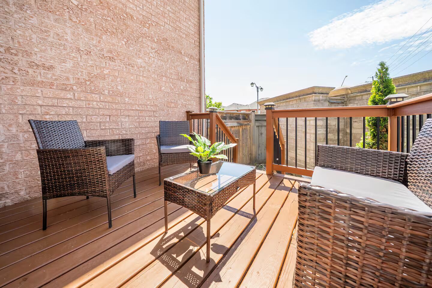A wooden deck with wicker furniture, a glass table, and a potted plant.