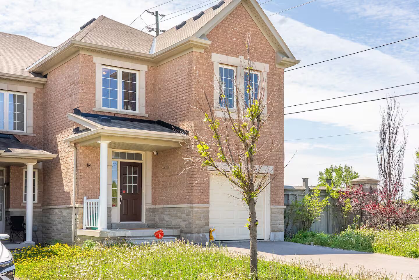 Une maison à deux étages avec une façade en briques, un porche à l’avant et un garage.