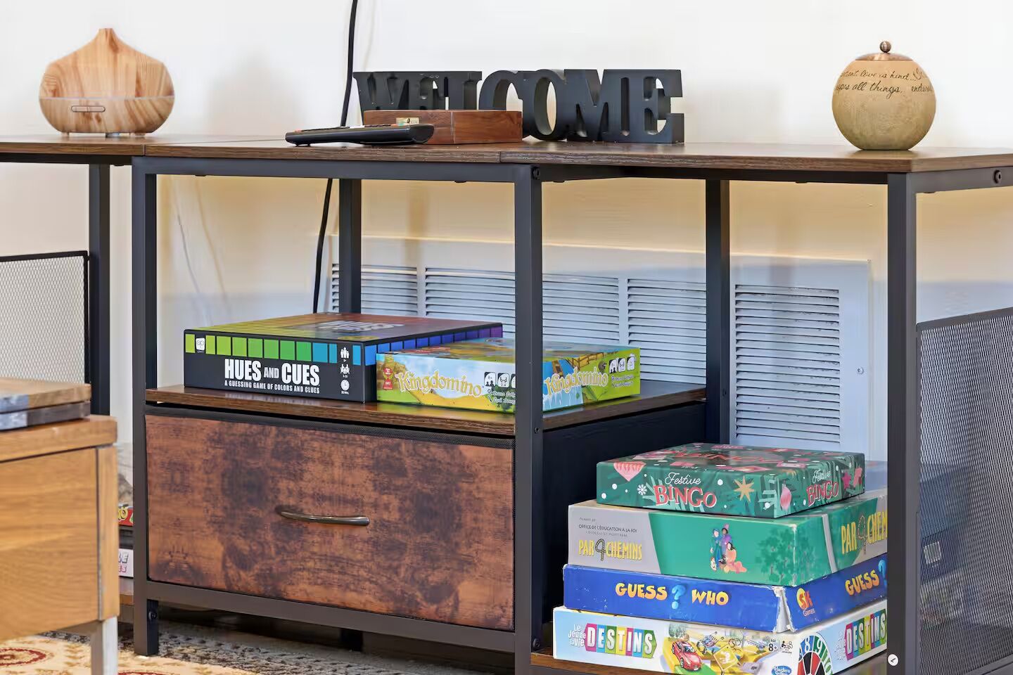 A wooden table with a 'WELCOME' sign, a diffuser, and various board games.