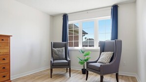 Une pièce comprenant deux fauteuils, une commode en bois, une fenêtre avec des rideaux et une plante en pot.