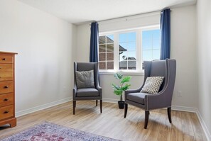 A room with two armchairs, a wooden dresser, a window with curtains, and a potted plant.
