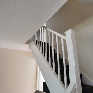 A white staircase with a textured ceiling and a dark carpeted landing. - Cozy & Stylish Home Near Manchester City. (Salford)