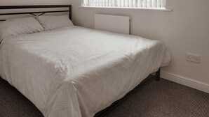 Una cama individual con cabecera, una ventana con persianas, un radiador y un enchufe en la pared.