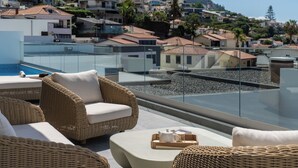 A terrace with wicker furniture, a pool, and a view of a hillside residential area.