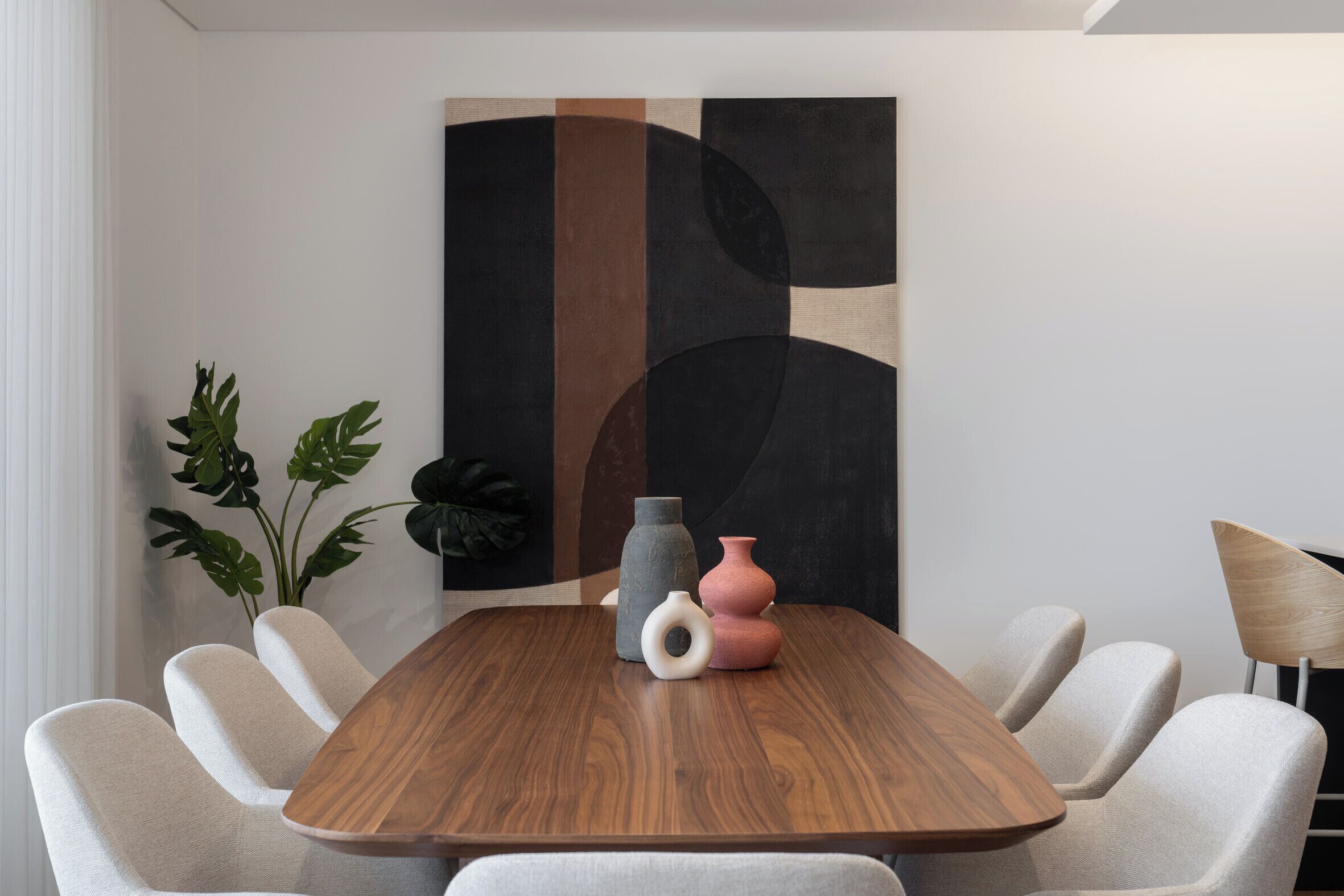Ein moderner Essbereich mit einem Holztisch, sechs gepolsterten Stühlen und einem großen abstrakten Gemälde an der Wand.