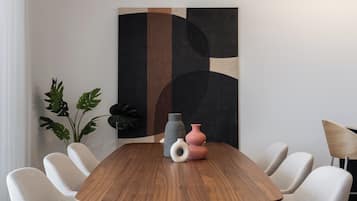 Un espace repas moderne avec une table en bois, six chaises rembourrées et un grand tableau abstrait accroché au mur.