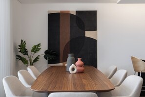 Uma área de refeições moderna com uma mesa de madeira, seis cadeiras estofadas e um grande quadro abstrato na parede.