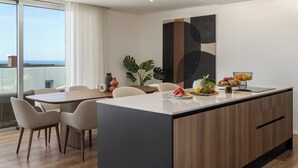 A modern kitchen with a central island, dining area with chairs, and a view of the ocean.