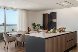 A modern kitchen with a central island, dining area with chairs, and a view of the ocean.