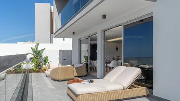 Eine moderne Lounge-Bereich im Freien mit Korbmöbeln, einer Glastür, die zu einem Innenraum führt, und Blick auf den Himmel.