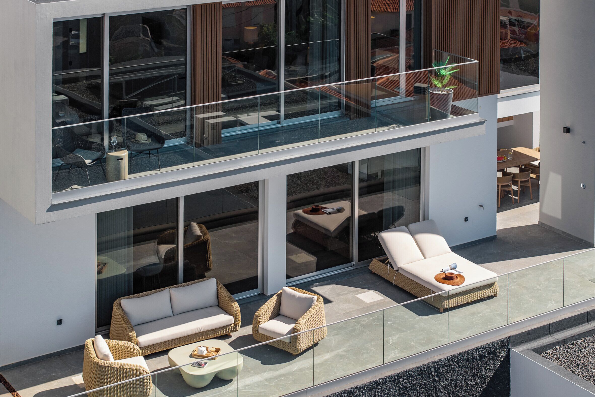 A modern two-story building with a glass balcony, wicker furniture, and a dining area.