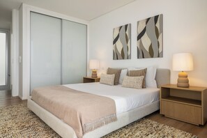 Quarto moderno com uma cama grande, duas mesas de cabeceira com luminárias, uma porta deslizante e arte abstrata na parede.