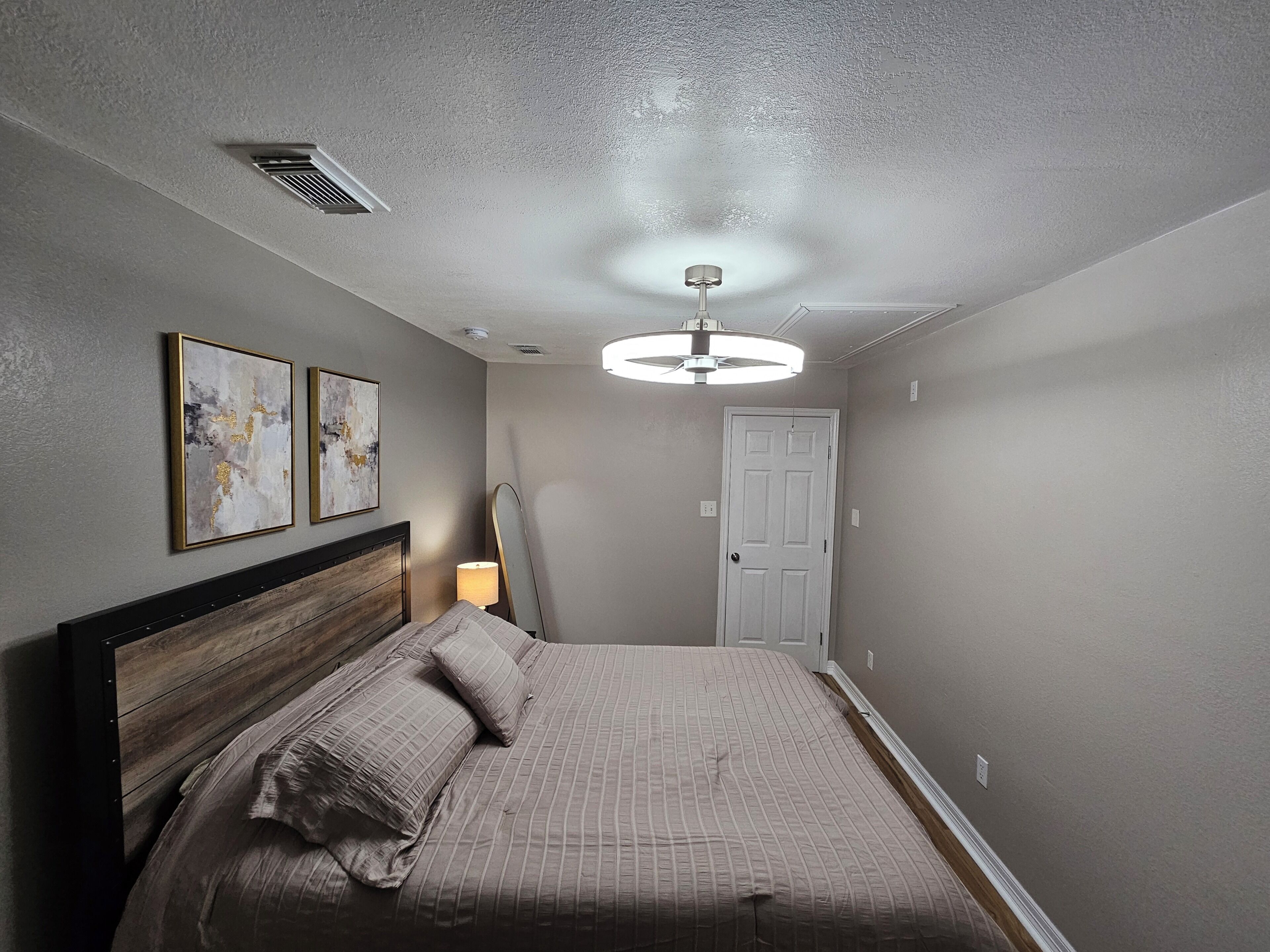 A bedroom with a bed, a ceiling fan, a door, and two wall-mounted artworks.