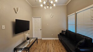 Ein Wohnzimmer mit Flachbildfernseher, einer schwarzen Ledersofa, Holzboden, einem Glastisch und einem modernen Kronleuchter.