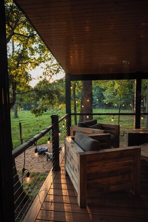 An outdoor seating area with a wooden bench and a table, surrounded by a wooden deck and a railing. - Bison Farm - Cabin "Cielo" (Culpeper)