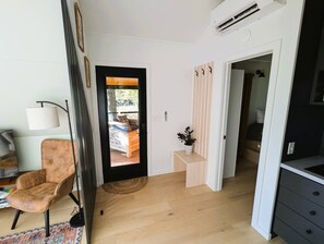 A modern interior with a wooden floor, a seating area with a chair, a small table, and a doorway leading to another room. - Bison Farm - Cabin "Cielo" (Culpeper)
