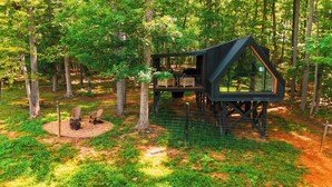Ein Baumhaus mit einer Terrasse und einer Glaskonstruktion, umgeben von einem Wald.