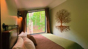 Ein Zimmer mit einem Bett, einem fensterbelaubten Fenster, einer Wandlampe und einer Baummalerei.