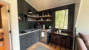 A compact kitchen with a microwave, coffee maker, and a window with a view of trees.