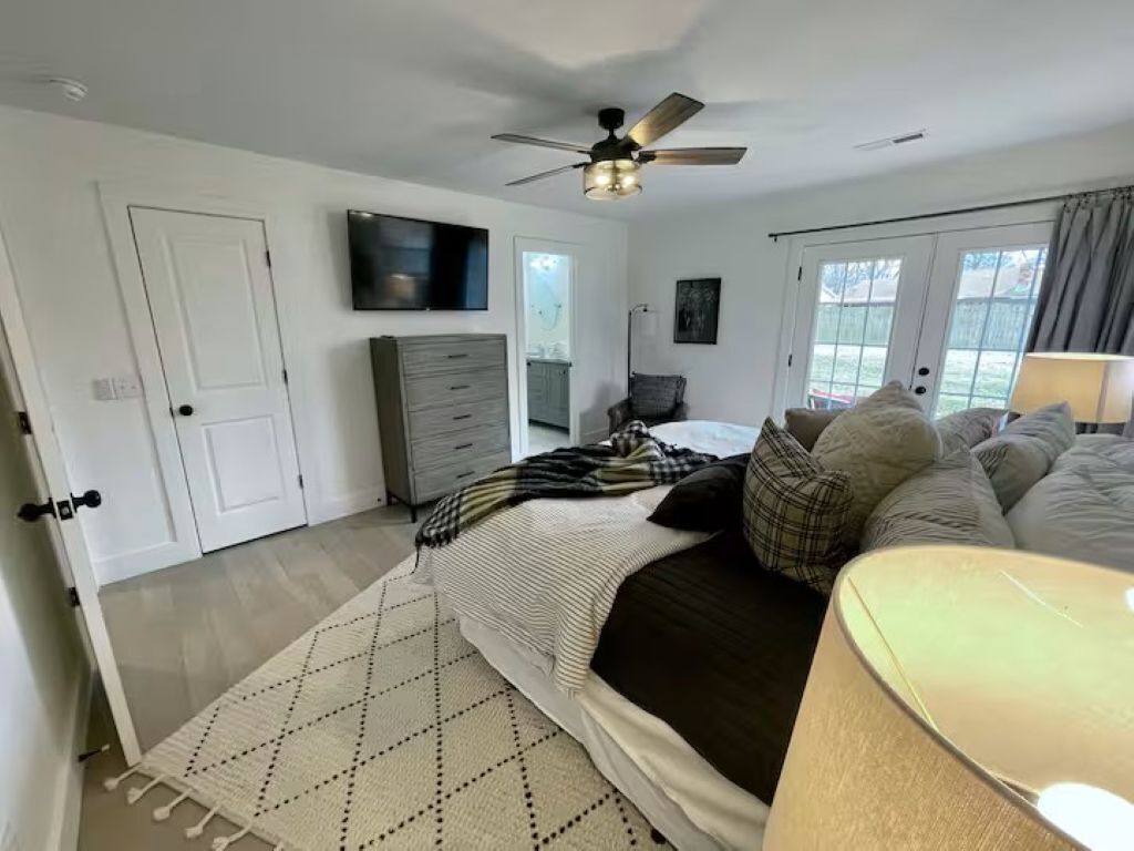 Un dormitorio con cama, ventilador de techo, televisor, cómoda y ventana.