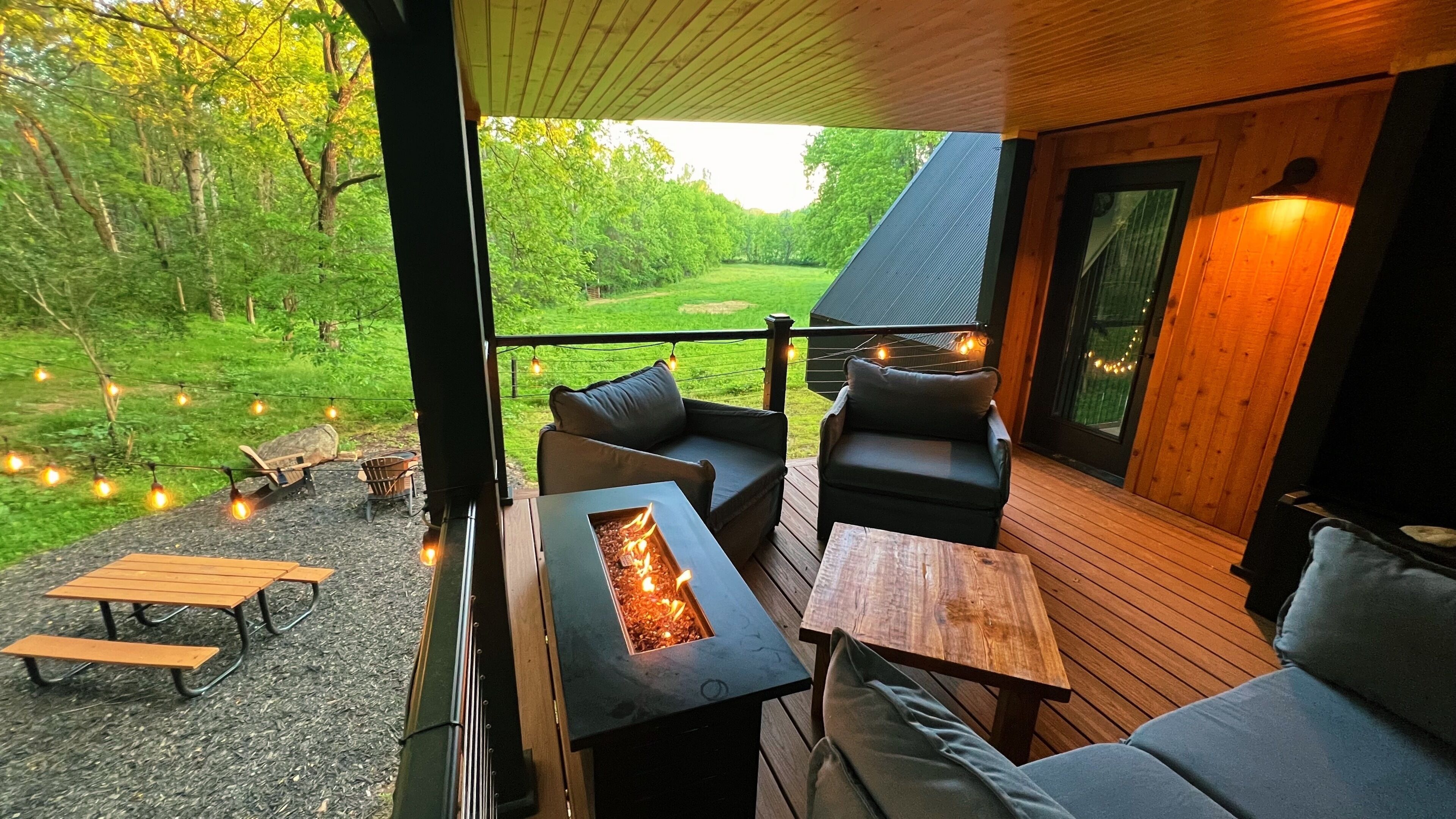 A covered outdoor seating area with a fire feature, wooden tables, and benches.