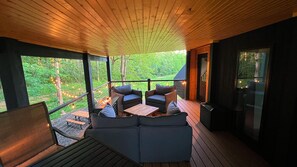 An outdoor deck with a wooden ceiling, a seating area with sofas and a table, and a view of a forested landscape. - Bison Farm - Cabin "Loma" (Culpeper)