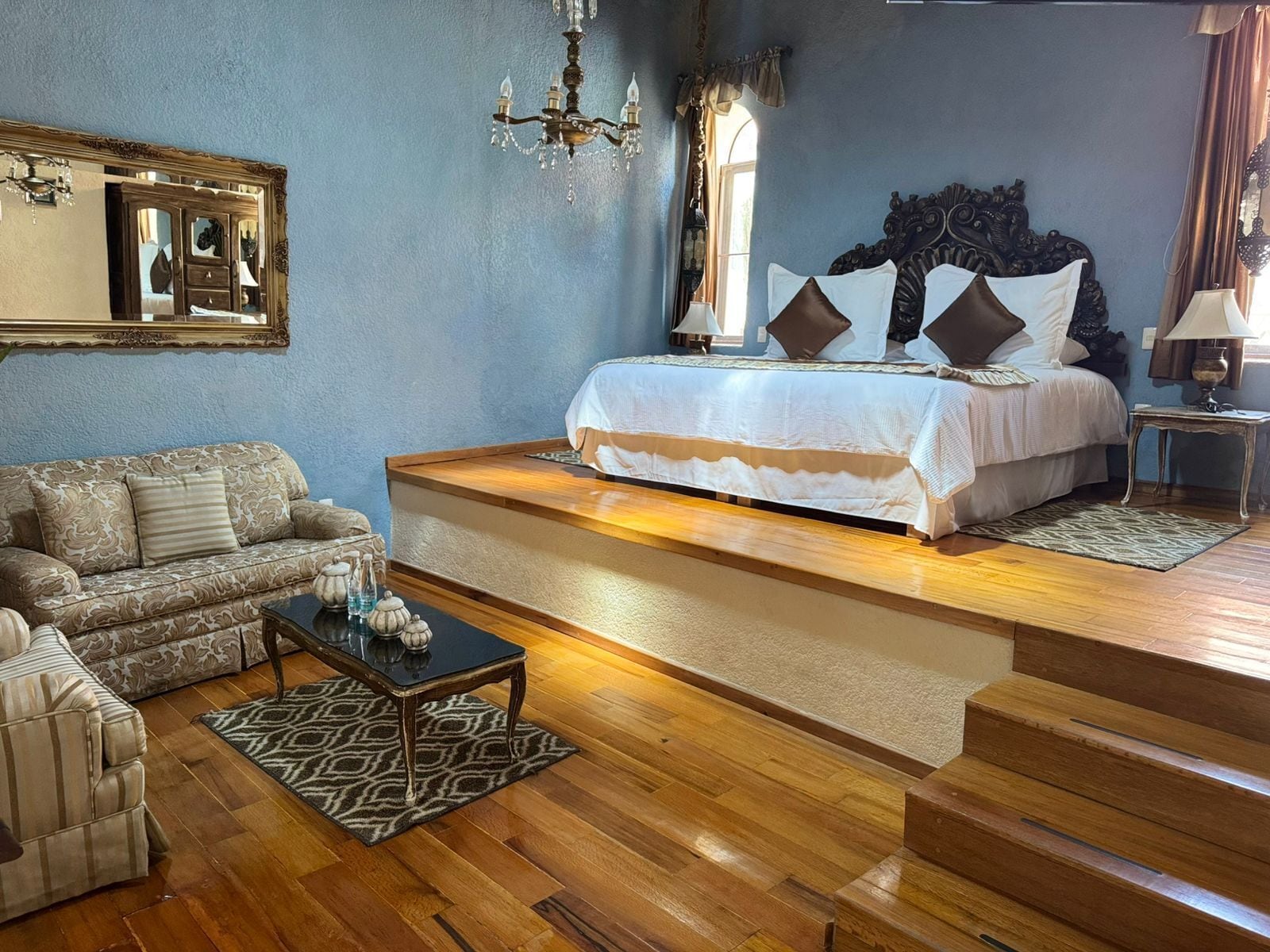 Un dormitorio con cama, sofá, una mesa de centro y un espejo.