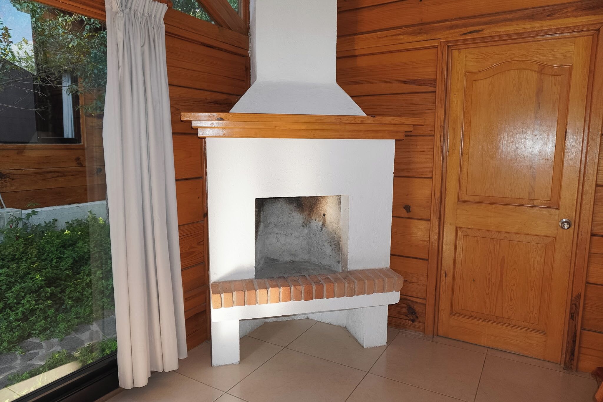 Una habitación con paneles de madera, una chimenea, una puerta y un ventanal con cortinas.