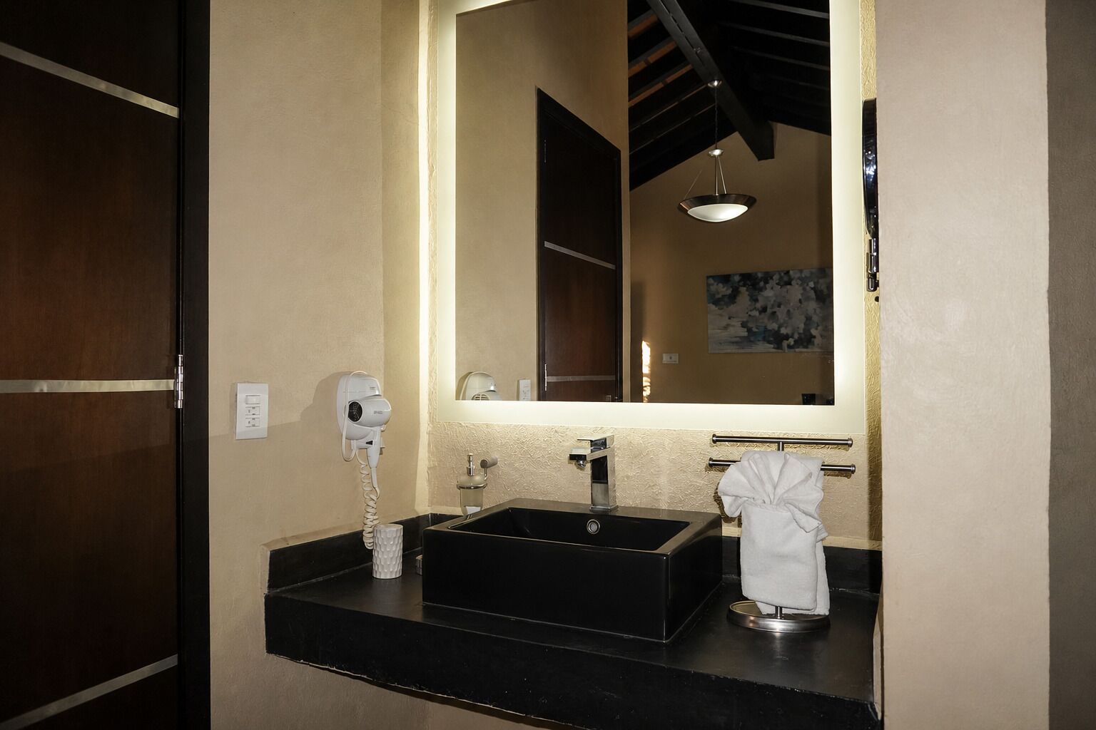 Un baño con un lavamanos negro, un espejo, un secador de pelo y un perchero para toallas.