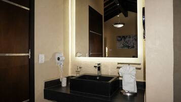 Un baño con un lavamanos negro, un espejo, un secador de pelo y un perchero para toallas.